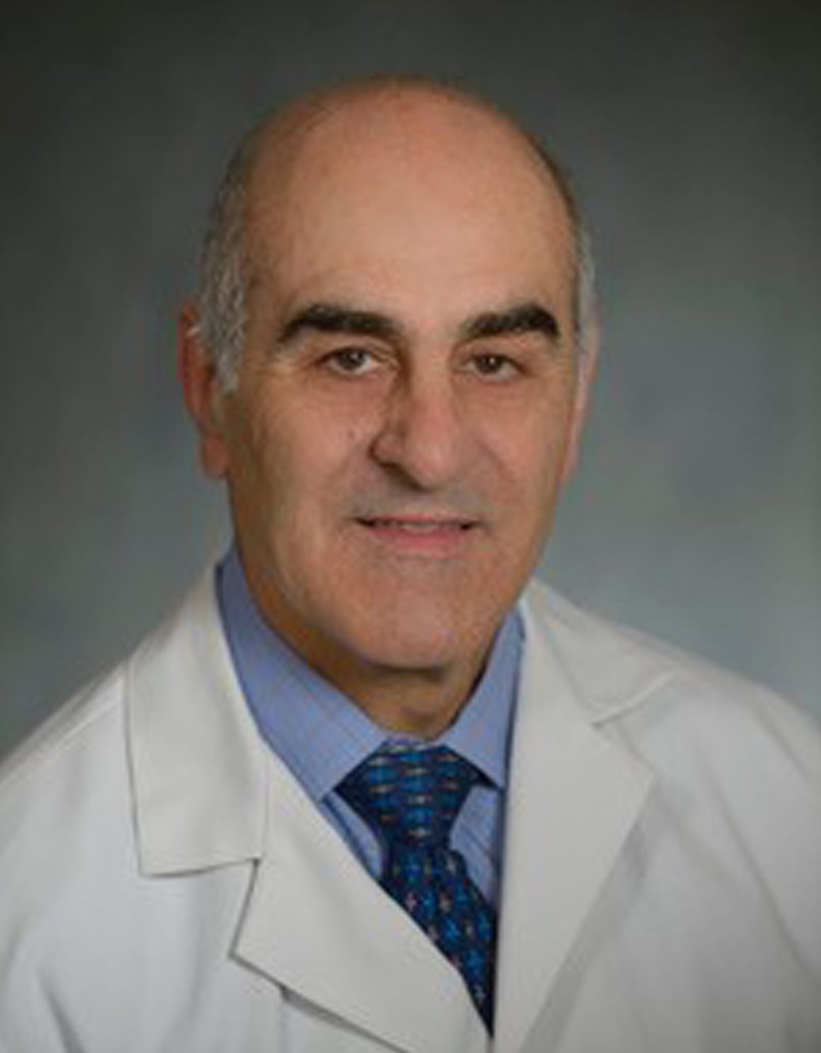 Male doctor in a white lab coat and blue shirt smiling at the camera.